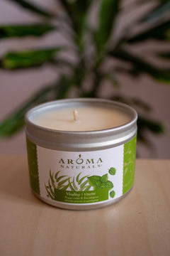 Peppermint and eucalyptus Aroma Naturals soy candle tin photographed with a blurred green plant background.
